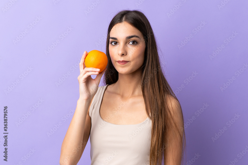 Young caucasian woman isolated on purple background holding an orange Young caucasian woman isolated on purple background holding an orange