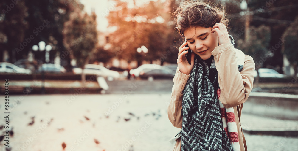 Fototapeta premium Pretty teen girl strolling on a square full of doves, talking on phone and enjoying the last warm days in a year.