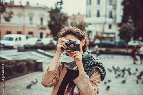 Young female tourist visiting old town on vacation and taking photos on old camera on the street.