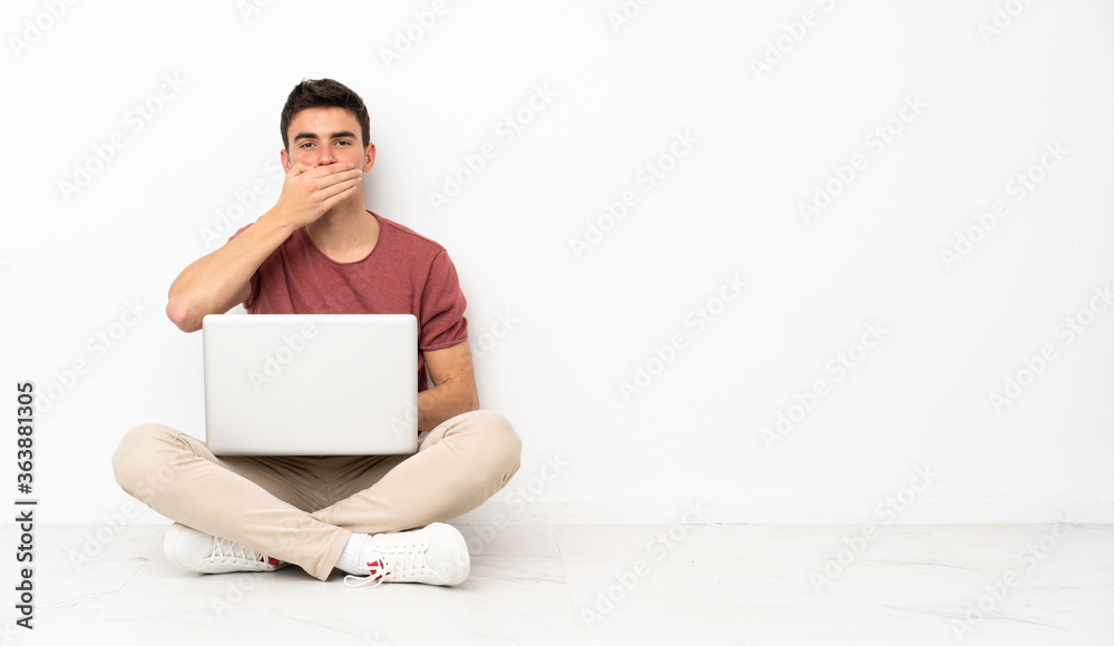 Teenager man sitting on the flor with his laptop covering mouth with hands Teenager man sitting on the flor with his laptop covering mouth with hands