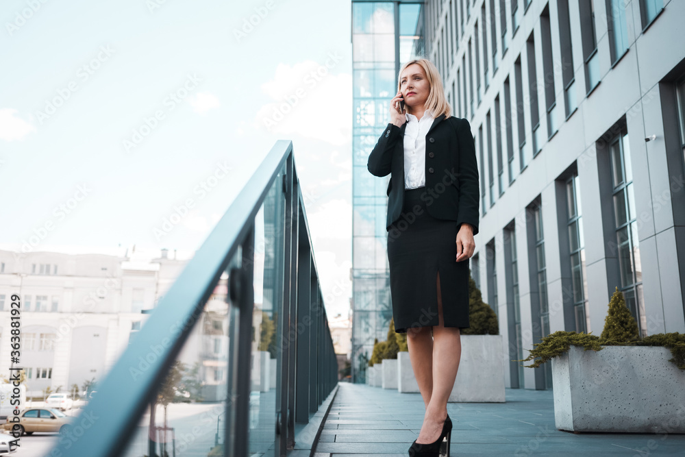 Serious business woman talking on the smartphone while standing near an office building Serious business woman talking on the smartphone while standing near an office building