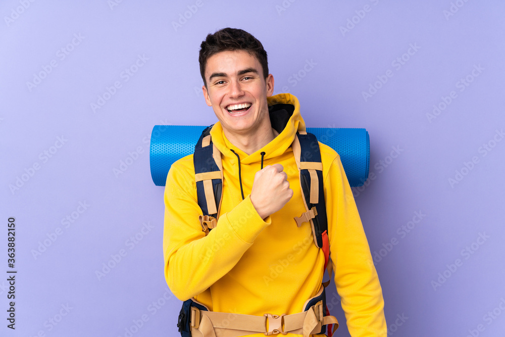 Teenager caucasian mountaineer man with a big backpack isolated on purple background celebrating a victory Teenager caucasian mountaineer man with a big backpack isolated on purple background celebrating a victory