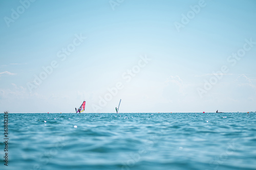 Windsurfers in the sea on sunset on horizon. Close up of sea wave, low angle view. Selective focus, bokeh