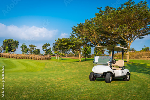 Golf cart on golf course, parking on fairway. Equipment and golf club bag are put in ready for golfer to player in field with sunlight rays background