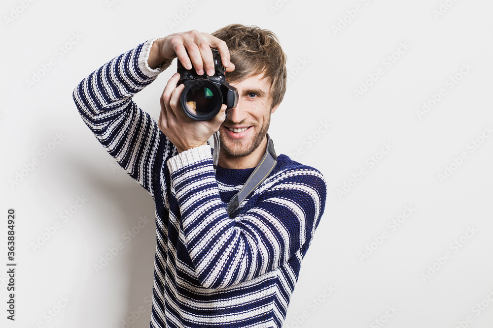 Young cheerful man photographer takes images with digital camera isolated on white background. Studio shot. Travel, photography, professional freelance work, hobby and active lifestyle concept Young cheerful man photographer takes images with digital camera isolated on white background. Studio shot. Travel, photography, professional freelance work, hobby and active lifestyle concept
