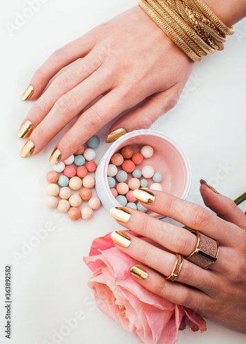 woman hands with golden manicure and many rings holding brushes  makeup artist stuff stylish  pure closeup pink flower rose among cosmetic for makeup