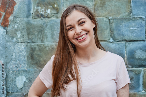 Smiling young woman in pink t-shirt on gray wall background