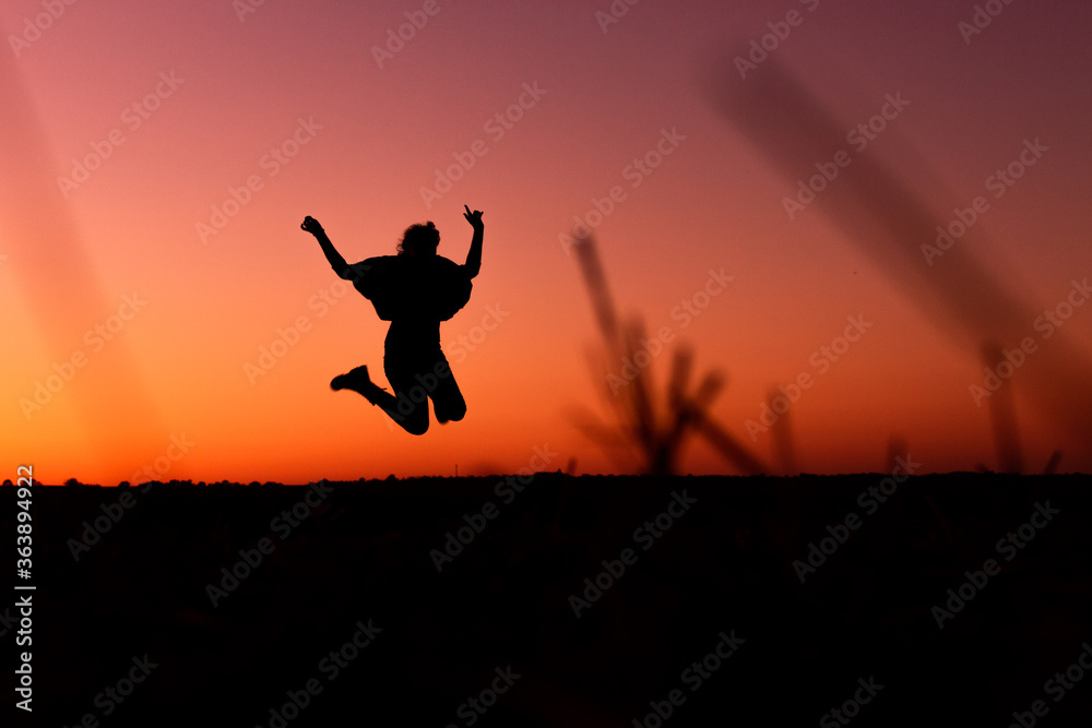 A silhouette of a happy woman who is jumping in front of a sunset