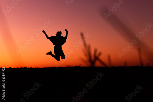 A silhouette of a happy woman who is jumping in front of a sunset