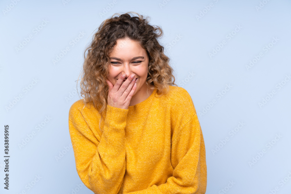 Young blonde woman with curly hair isolated on blue background smiling a lot