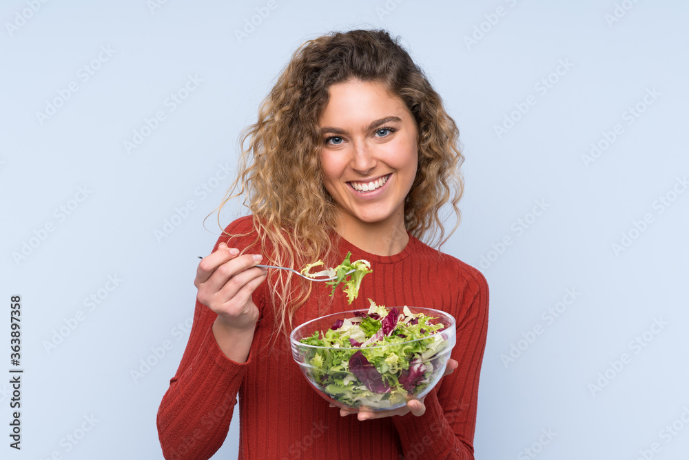 Young blonde woman with curly hair holding a salad over isolated wall Young blonde woman with curly hair holding a salad over isolated wall