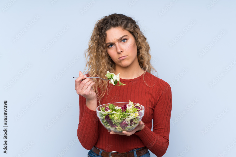Young blonde woman with curly hair holding a salad over isolated wall Young blonde woman with curly hair holding a salad over isolated wall