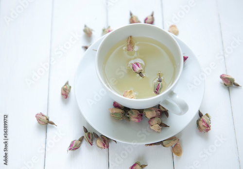 Herbal, rose-flavored tea in a white cup with scattered tiny dried rose buds. A mediterranean herbal tea shot from above angle