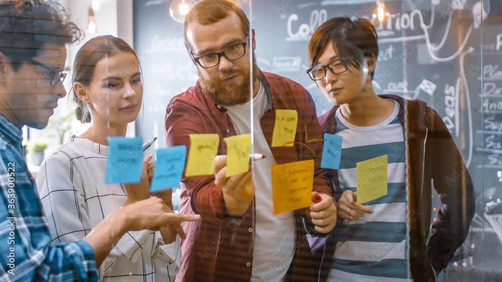 Obraz premium Diverse Team of Young Developers Brainstorming, They Have Discussion and Use Glass Board and Sticky Papers to Conceptualize Their New Plan. Creative People in Stylish Office Environment.