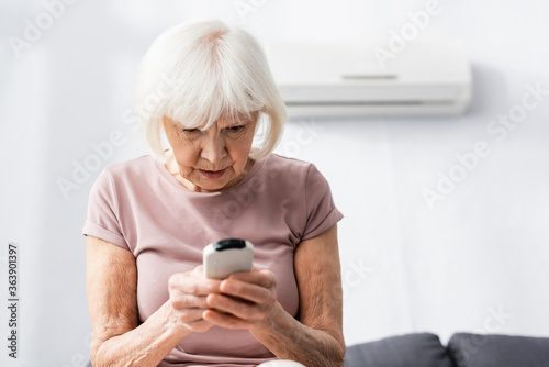 Selective focus of elderly woman holding remote controller of air conditioner at home