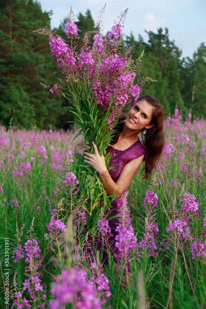 Smiling young woman holding the bouquet of pink flowers. Pink Ivan Tea or blooming Sally in the field Smiling young woman holding the bouquet of pink flowers. Pink Ivan Tea or blooming Sally in the field