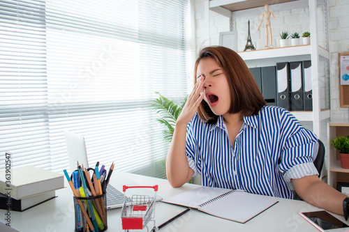 Woman yawning and sleepy at an office desk, overwork and sleep deprivation concept.