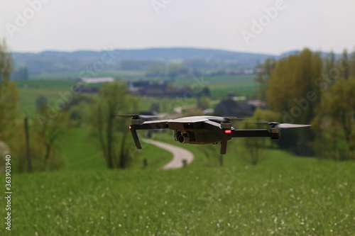 A generic drone hoovering over a beautiful meadow, with a curvy road in a landscape on the background. The camera is under the rotating blades. Flying a drone is the newest hype in aviation technology