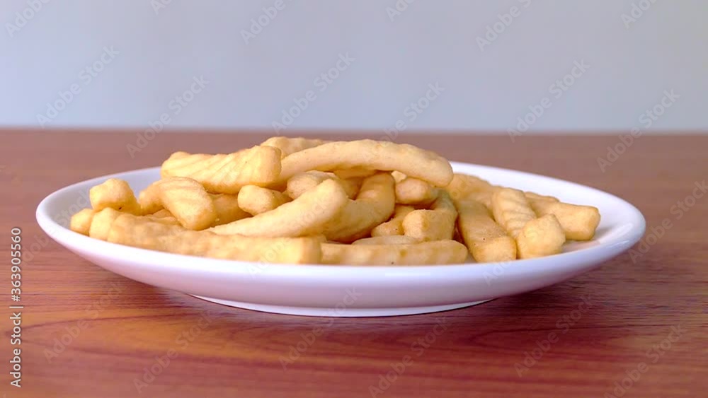 The hand picked the crackers in a white plate on a wooden table