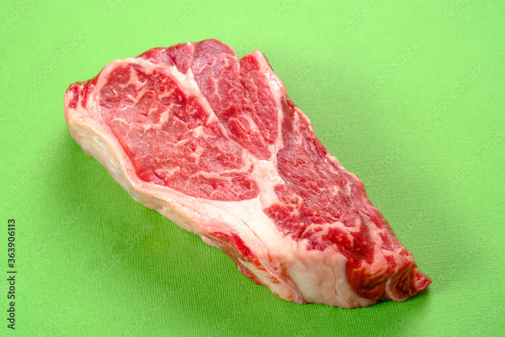 Fresh raw beef steak on a green background
