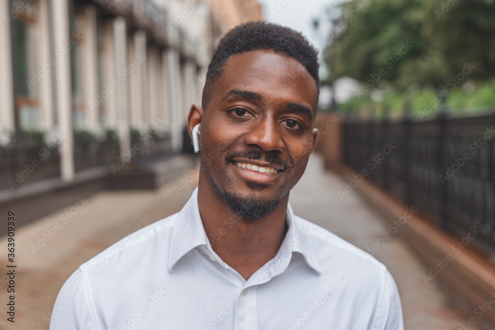 Portrait of a smiling black businessman with wireless earphones walking outdoors Portrait of a smiling black businessman with wireless earphones walking outdoors