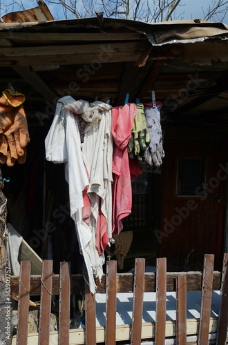 Washed laundry hanging in front of poor, old house. Colorful laundry drying in sun, social scene. Workers clothes drying in poor house yard