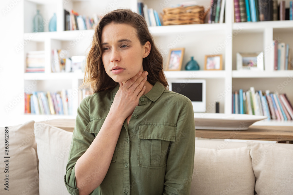 Woman with sore throat holding her neck at home Woman with sore throat holding her neck at home