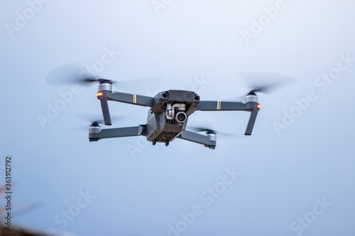 Focus on the modern small folding gray drone. The drone flies and shoots on the shores of the sea and behind you can see the blue sky.
