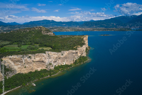 Lake Garda, Italy. Aerial view of punta sasso, rocca di manerba in the background mountains, san biagio island cumulus clouds at high altitude