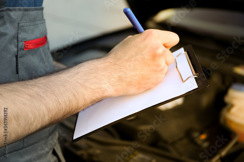 A man in overalls writes to a clipboard. Mechanic. Car inspection