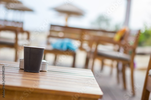 Focus on the black paper coffee cup on the table in the beach cafe. The cafe is empty and there are no people. copy space.