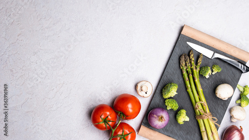 Group of organic fresh vegetables - green asparagus, broccoli, mushrooms on grey background, flat lay. Concept of  healthy vegetarian food, diet and home cooking.