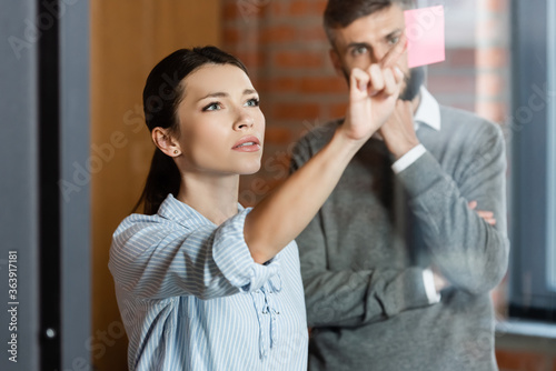 selective focus of businesswoman pointing with finger at sticky note near businessman