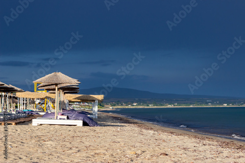 The dark blue sky is above the beach by the sea. It s like a storm. The beach is empty and there are no people.