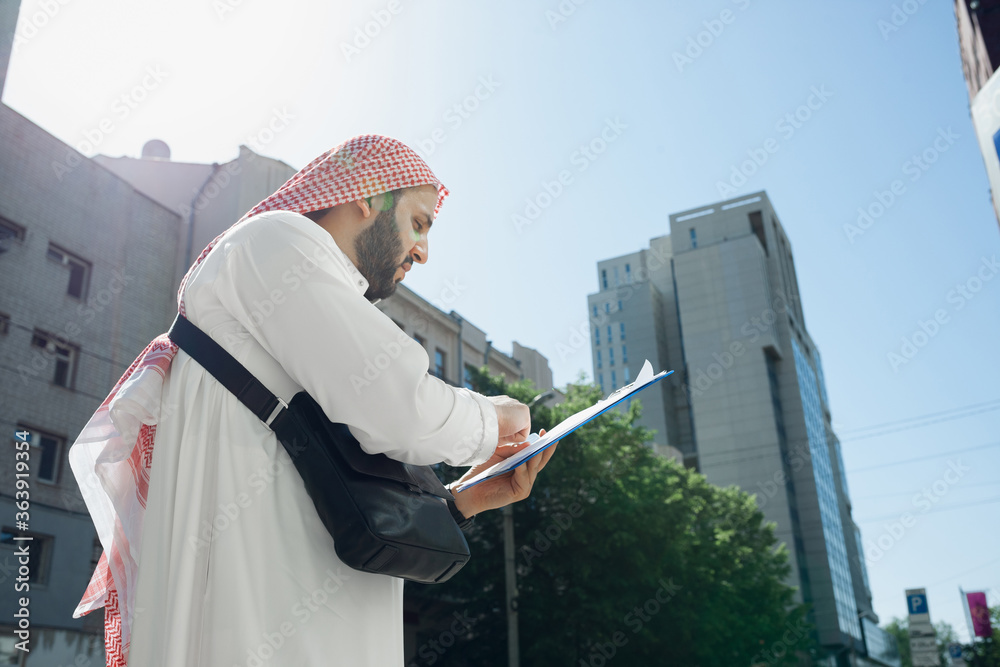 Agreement. Rich arabian man's portrait during buying real estate, business center in city. Ethnicity, culture. Confident man in traditional wear making a deal successful. Finance, economy. Agreement. Rich arabian man's portrait during buying real estate, business center in city. Ethnicity, culture. Confident man in traditional wear making a deal successful. Finance, economy.