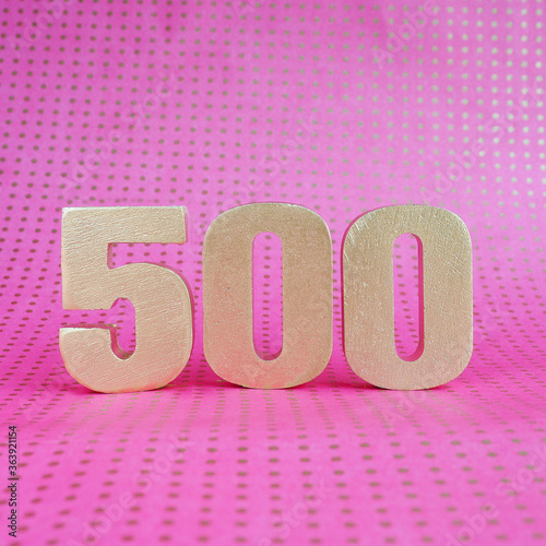 Gold volumetric number 500 on a bright pink polka dot background. copy space..