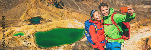 New Zealand Tongariro Alpine Crossing Hiking tourists couple selfie at Emerald Lakes. Happy backpackers tramping taking phone photo of themselves at volcanic mountains. Tramping track of New Zealand. photo