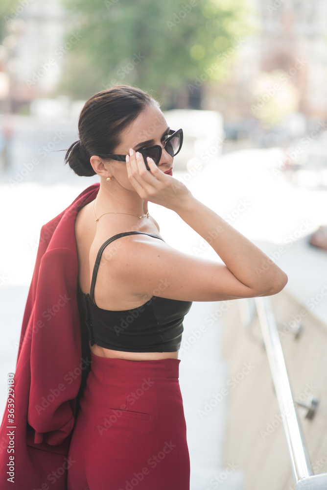 Woman in red dress and sunglasses standing on a street. Soft selective focus. Woman in red dress and sunglasses standing on a street. Soft selective focus.