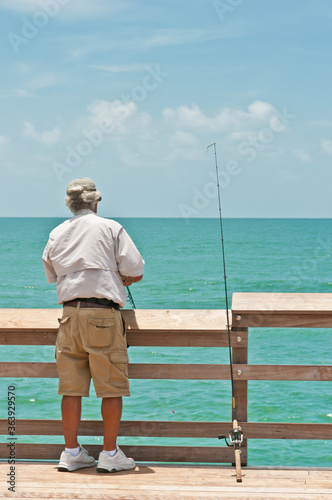 Back view, medium distance of a senior male fishing off a wood pier in the tropical waters of the gulf of Mexico on a sunny day