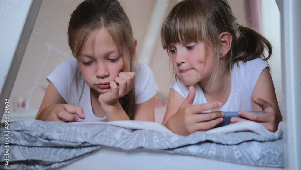 Happy little girl or child playing at home, relax, use a smartphone, sit on the couch daughter, look at the tablet screen, watch cartoons. Happy little girl or child playing at home, relax, use a smartphone, sit on the couch daughter, look at the tablet screen, watch cartoons.