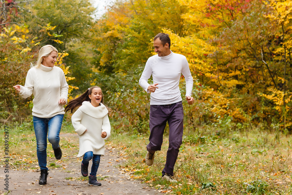 Fototapeta premium Picture of lovely family in autumn park, young parents with nice adorable daughter playing outdoors, have fun on backyard in fall, happy family enjoy autumnal nature