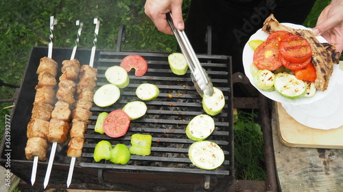 the cook removes vegetables and meat from the grill with tongs on a plate. delicious food.