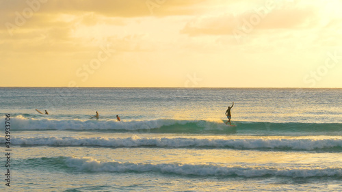 Male surfer catches a wave and rides it to coast on a sunny evening in Barbados