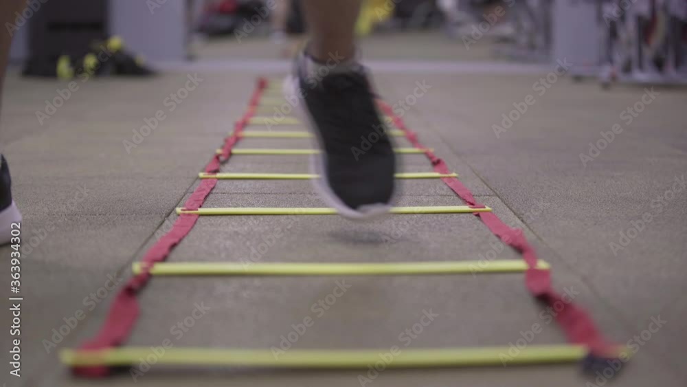 Male feet in sneakers stepping on ladder lying on the floor in gym. Close-up legs of unrecognizable Caucasian sportsman training indoors. Exercising, sport, healthy lifestyle concept. Male feet in sneakers stepping on ladder lying on the floor in gym. Close-up legs of unrecognizable Caucasian sportsman training indoors. Exercising, sport, healthy lifestyle concept.