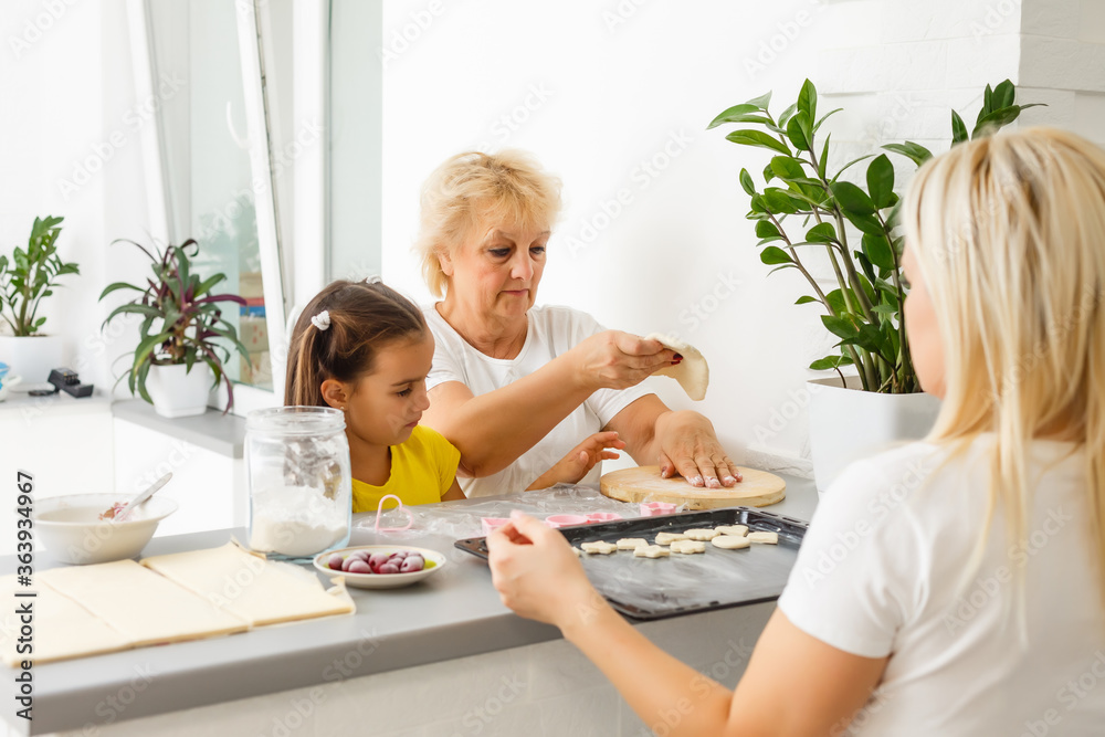 Little girl learning to roll dough and make homemade pastry or cookies with her mother and grandmother Little girl learning to roll dough and make homemade pastry or cookies with her mother and grandmother