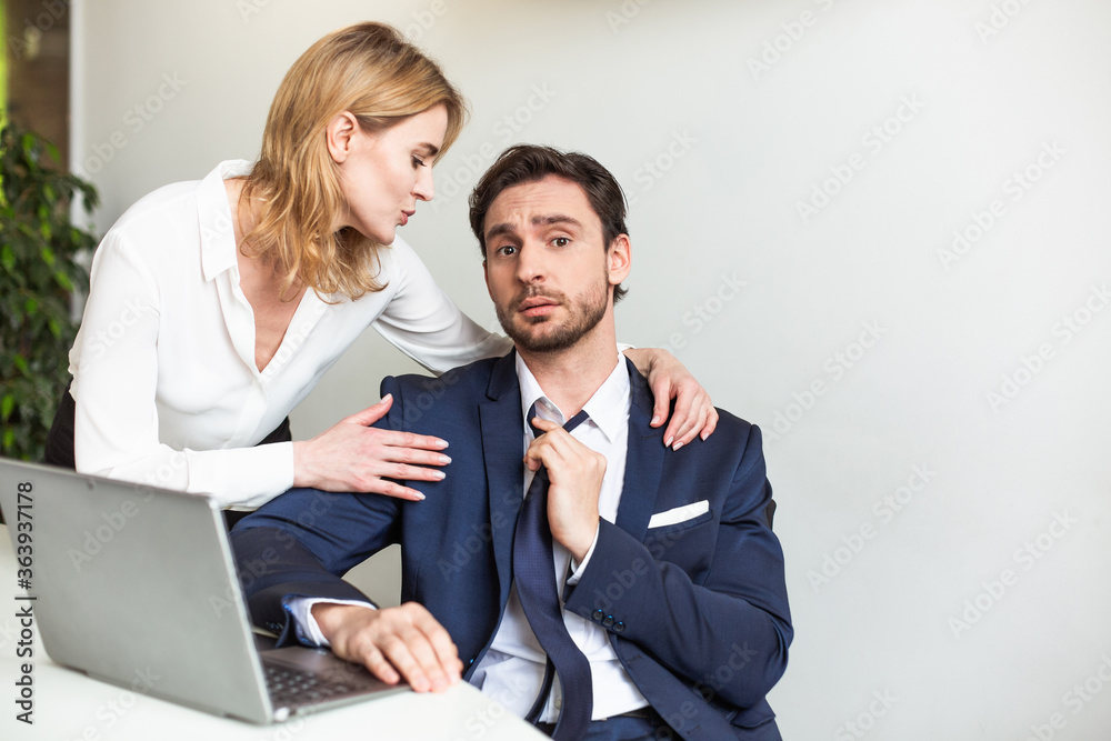 Blonde boss businesswoman seduces her male assistant working with laptop computer.Seducing a subordinate in office. Flirtation or sexual harassment. Blonde boss businesswoman seduces her male assistant working with laptop computer.Seducing a subordinate in office. Flirtation or sexual harassment.
