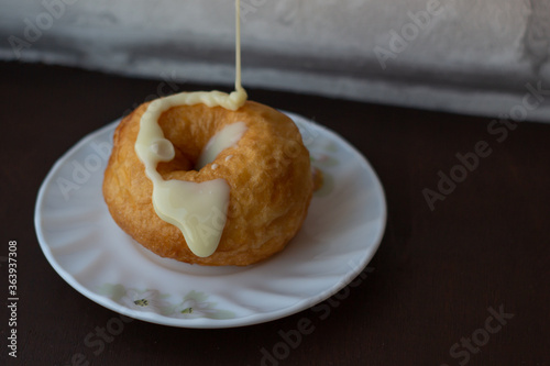 Big juicy donut being poured on with condensed milk photo