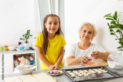 Cute little girl and her grandmother make cookies on kitchen.