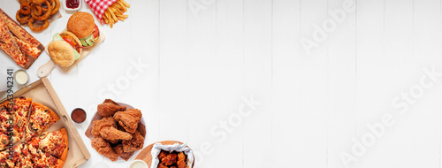 Selection of take out and fast foods. Corner border banner. Pizza, hamburgers, fried chicken and sides.  Top down view on a white wood background with copy space.