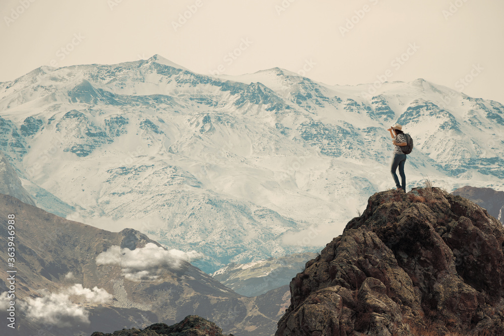 Foto de Mujer haciendo senderismo parada en la cima de una montaña muy  alta. Mira hacia abajo se ve un valle y nubes, de fondo la cordillera do  Stock